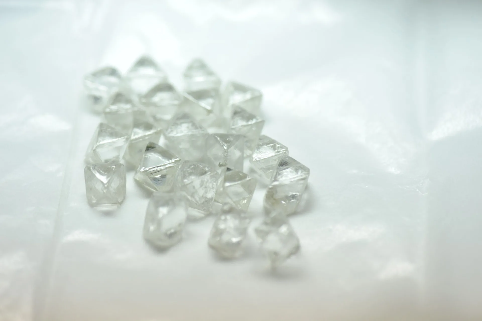 Natural rough diamond octahedrons arranged on white parcel paper.