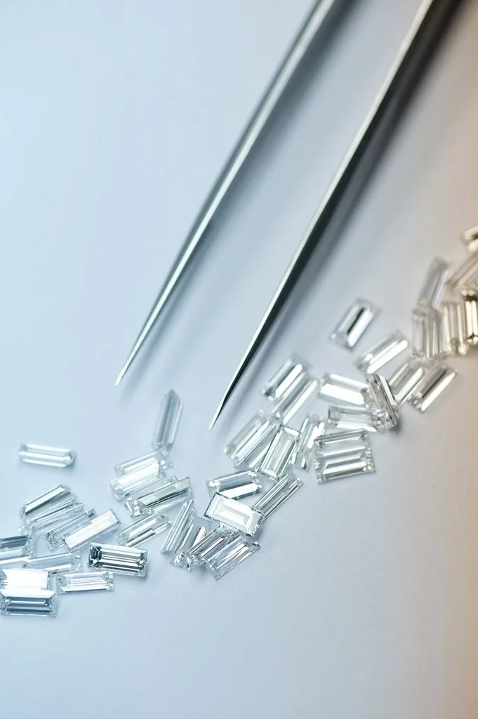 Calibrated baguette diamonds arranged beneath jeweller's tweezers.