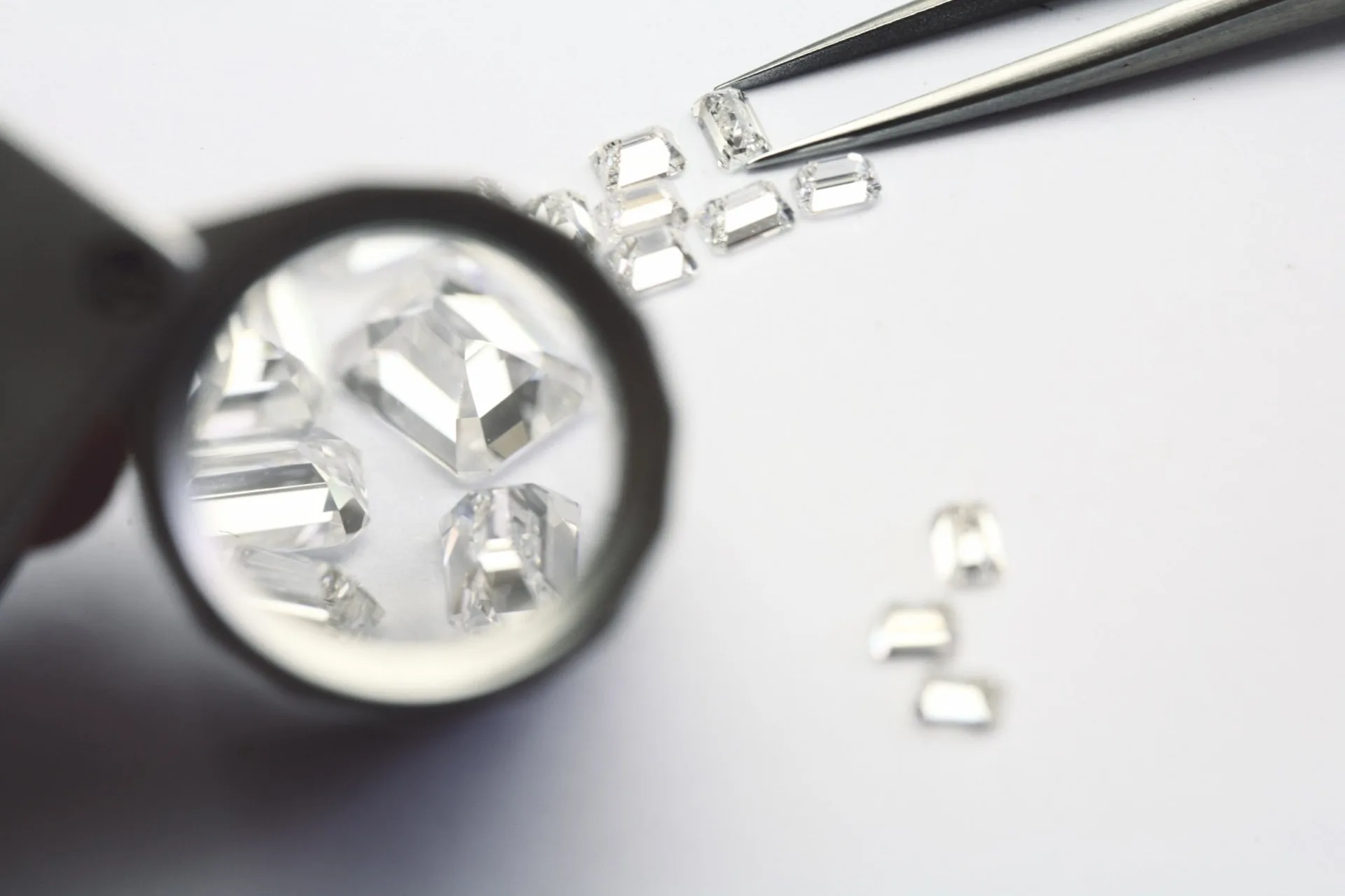 Emerald-cut diamonds viewed through a jeweller's loupe beside precision tweezers.