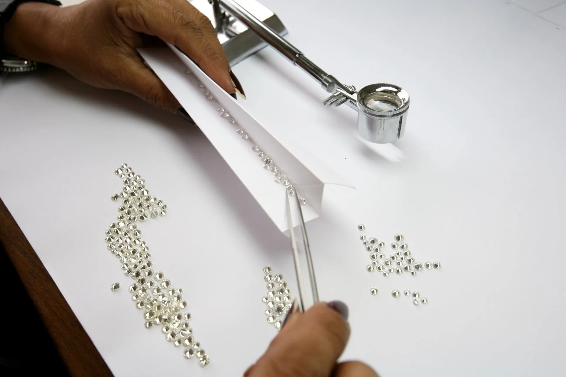 Diamonds being sorted by hand with a loupe and tweezers.