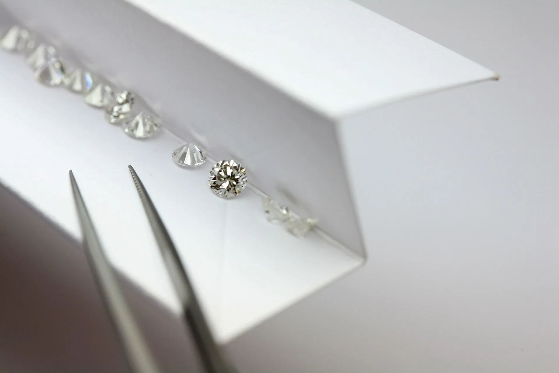 A calibrated line of round brilliant diamonds beside precision tweezers.