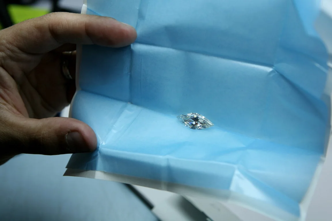 A marquise diamond presented in blue parcel paper by hand.
